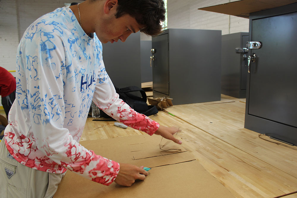 Design Discovery camper works on his cardboard chair project at a desk in Barn.
