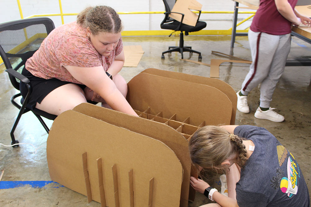 Design Discovery campers work on their cardboard chair project on the ground in Barn.