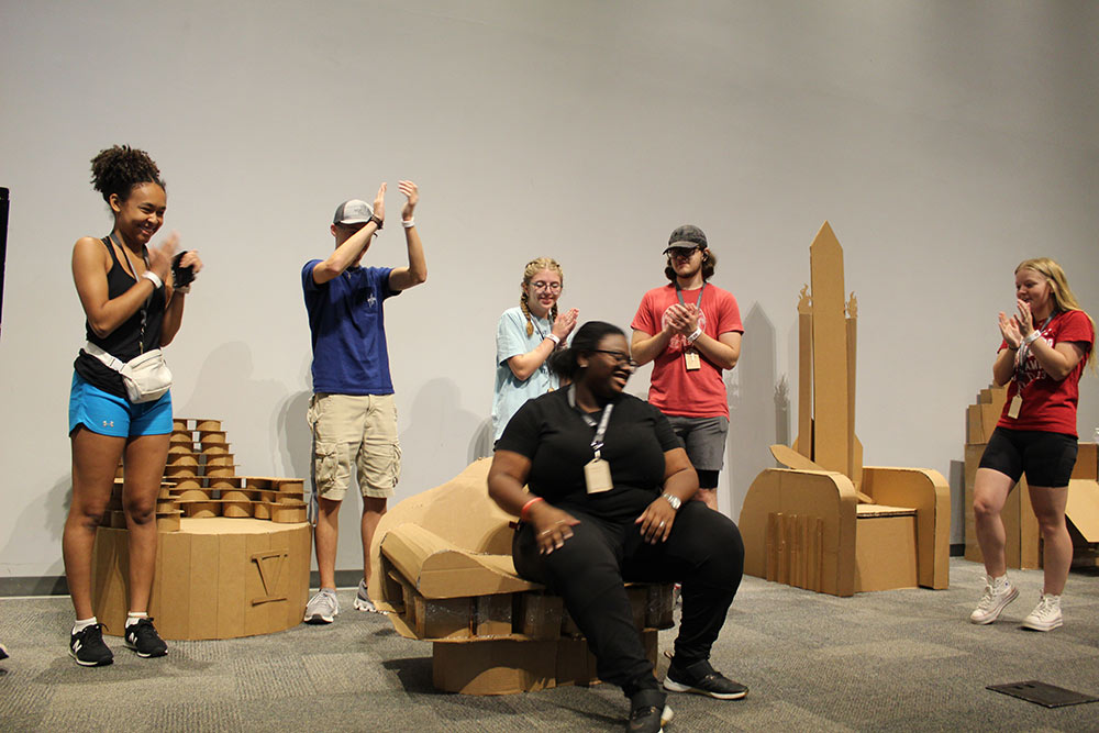 Group of campers cheering as one camper sits on their cardboard chair project.