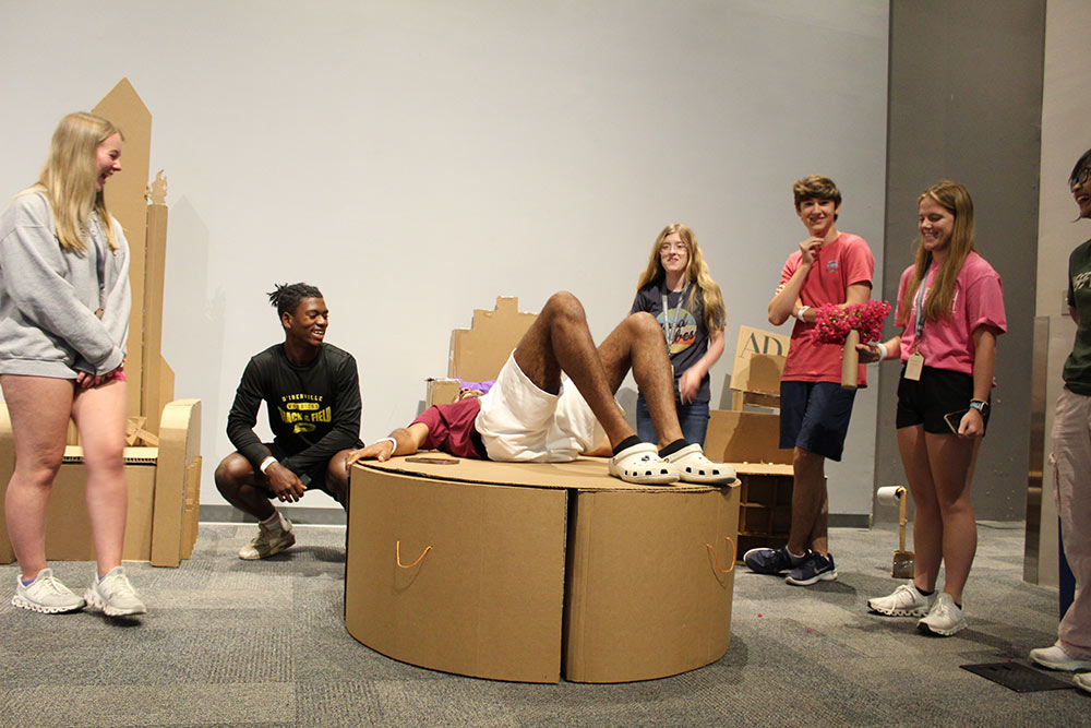 Group of campers laugh as one camper lays on their cardboard chair project.