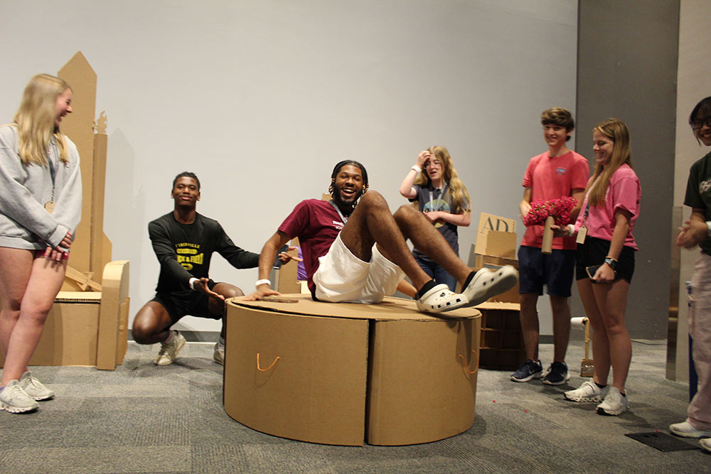 Group of campers laugh as one camper lays on their cardboard chair project.