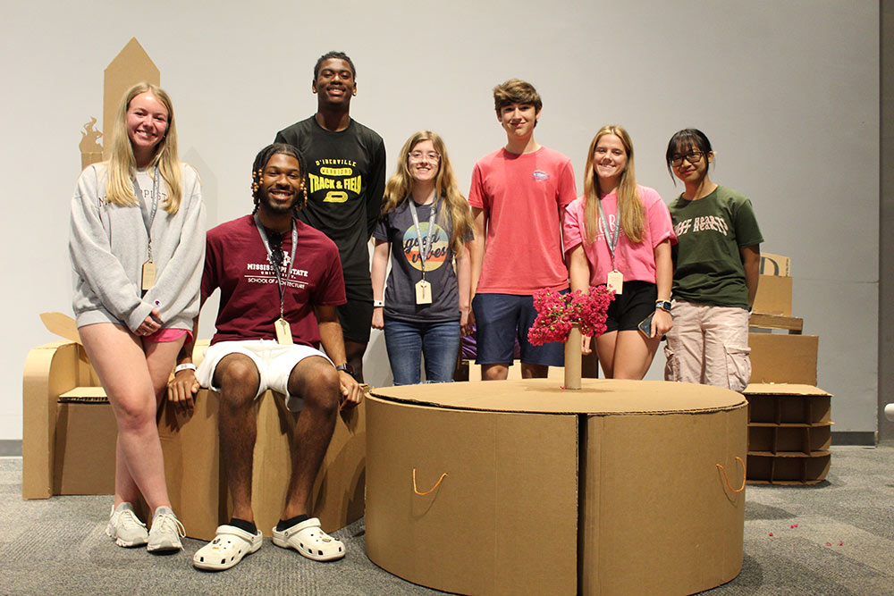 Group of campers pose around their cardboard chair project.