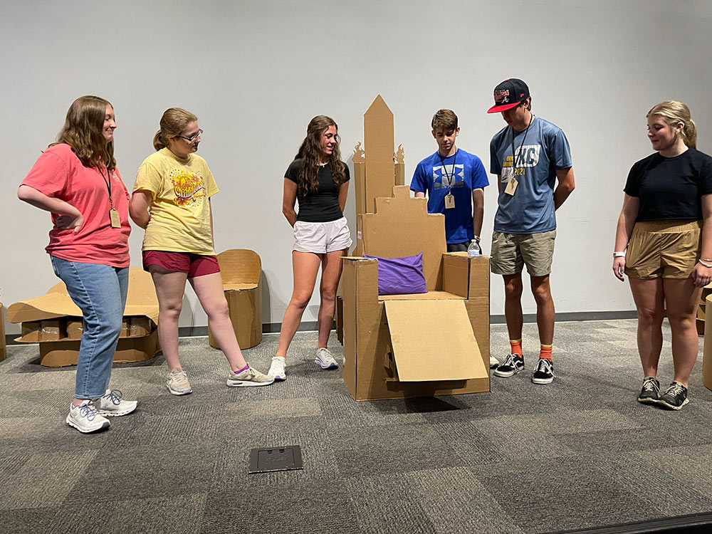 Group of campers stand around their cardboard chair project
