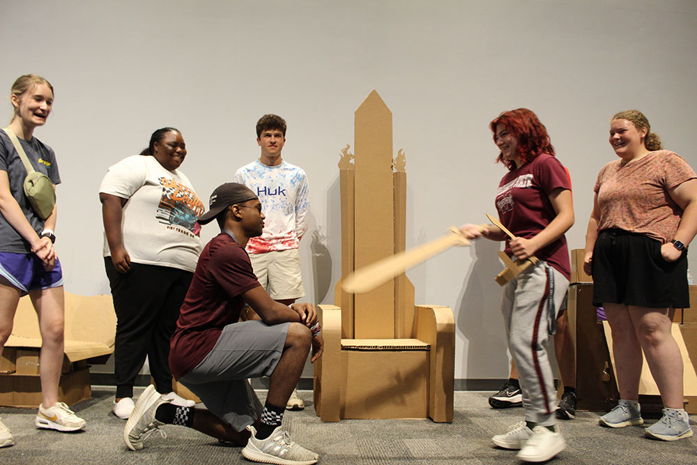 Group of campers stand around their cardboard chair project, one is holding a cardboard sword.
