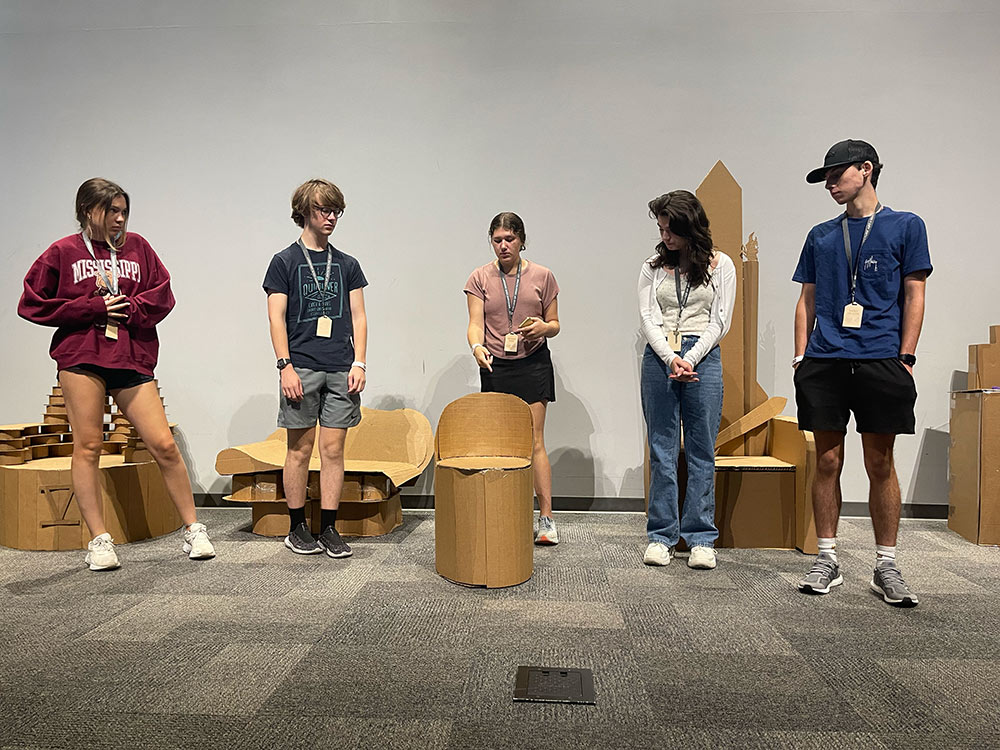 Group of campers stand around their cardboard chair project .