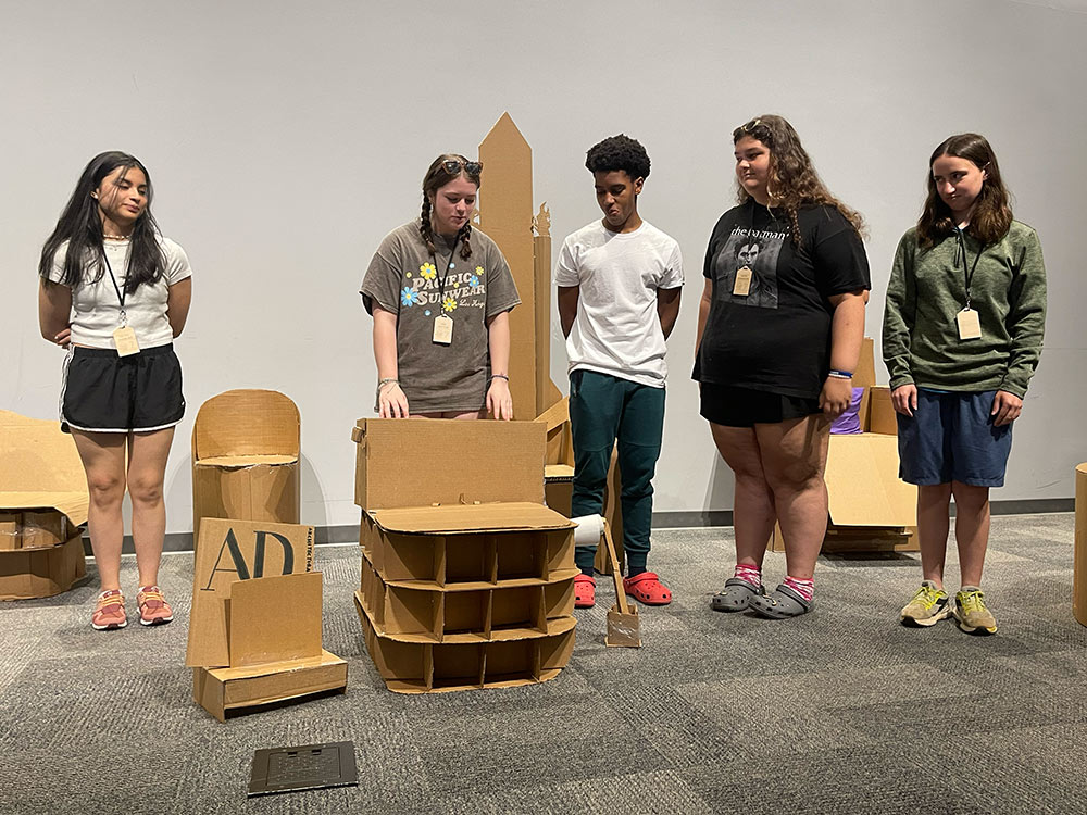 Group of campers stand around their cardboard chair project.