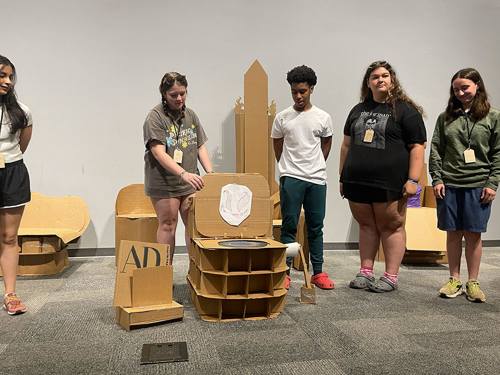 Group of campers stand around their cardboard chair project .