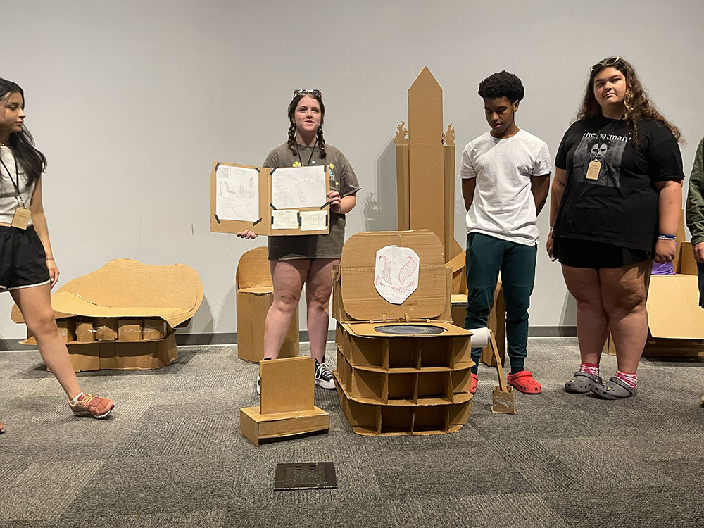 Group of campers stand around their cardboard chair projects.
