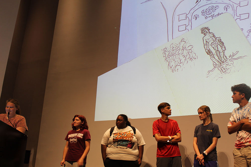 A group of Design Discovery campers presenting their sketches on the projector in the auditorium.