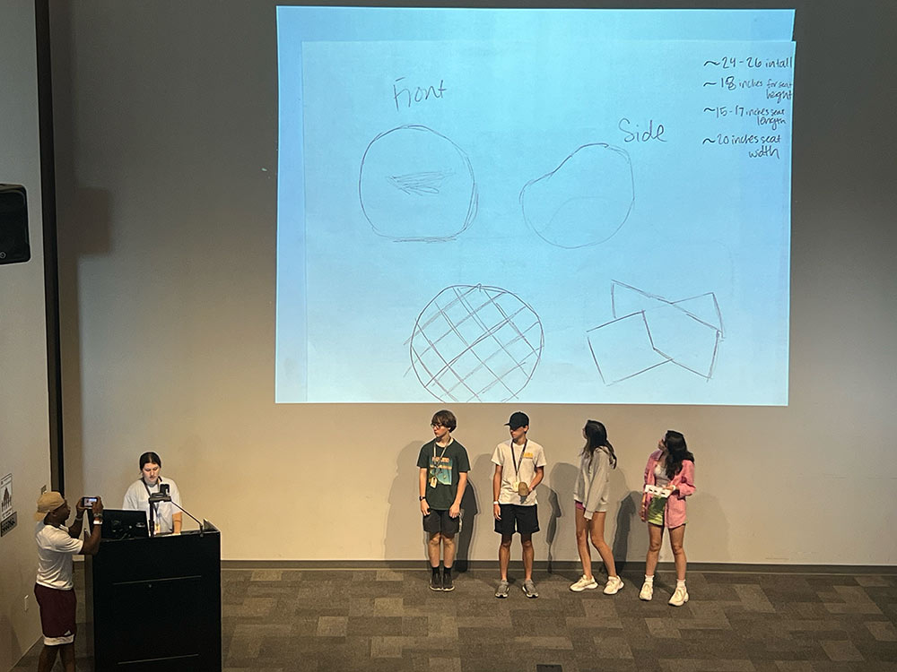 Design Discovery campers presenting their sketches on the projector to an auditorium full of other campers.