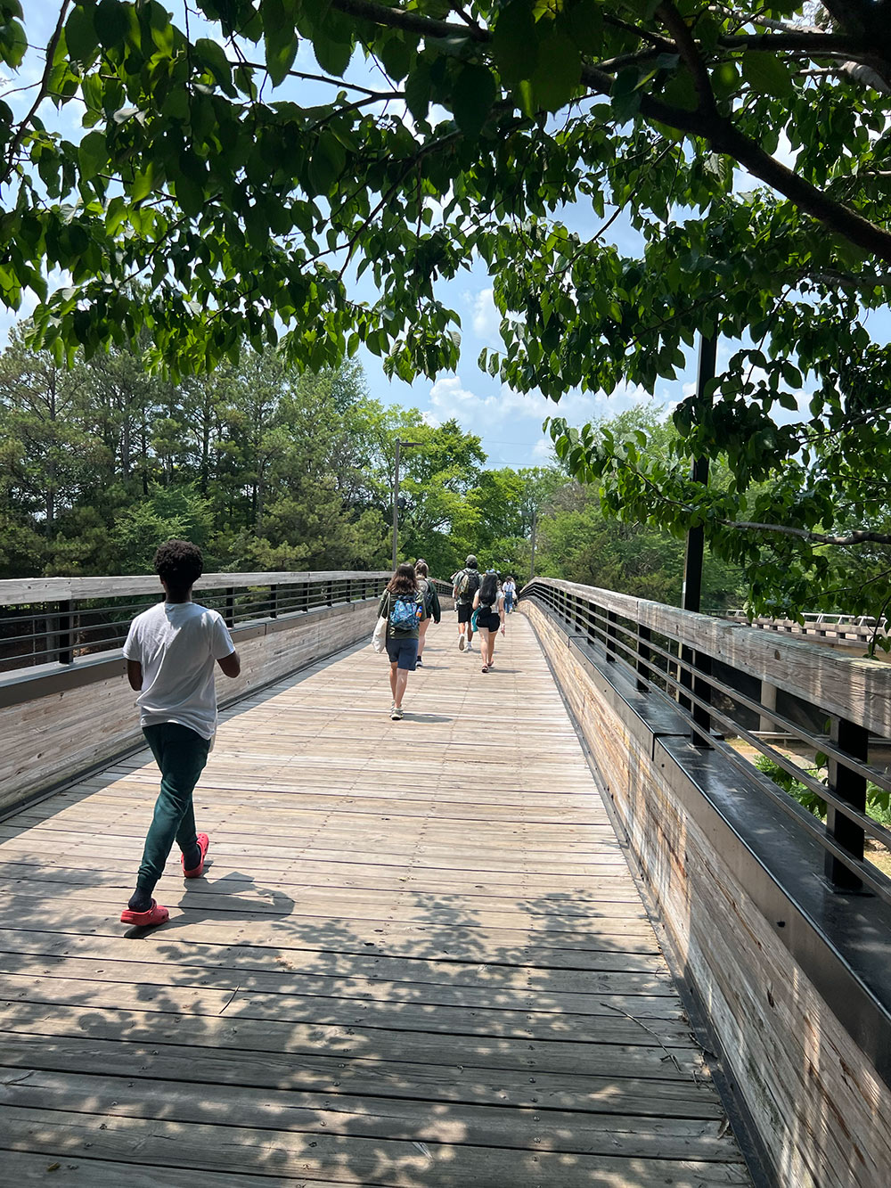 Group of Design Discovery campers walking across a wooden bridge outside.
