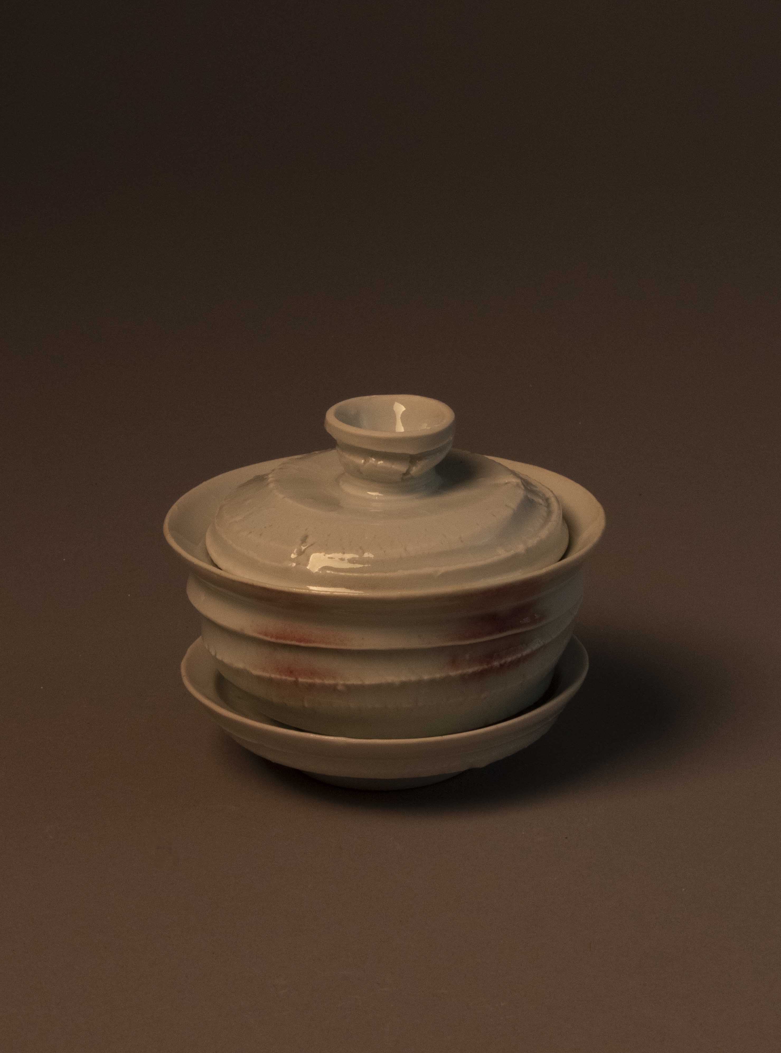 A three-part vessel for steeping tea – consisting of a saucer, a bowl-shaped cup with an outward-flaring lip, and a lid with a knob. The exterior surfaces have some slightly abrasive ridges and texture from the stretching of the clay during throwing. The slight roughness contrasts the delicacy of the vessel (evident in the apparent thinness of the rims of the cup and saucer), and the glassy glaze.