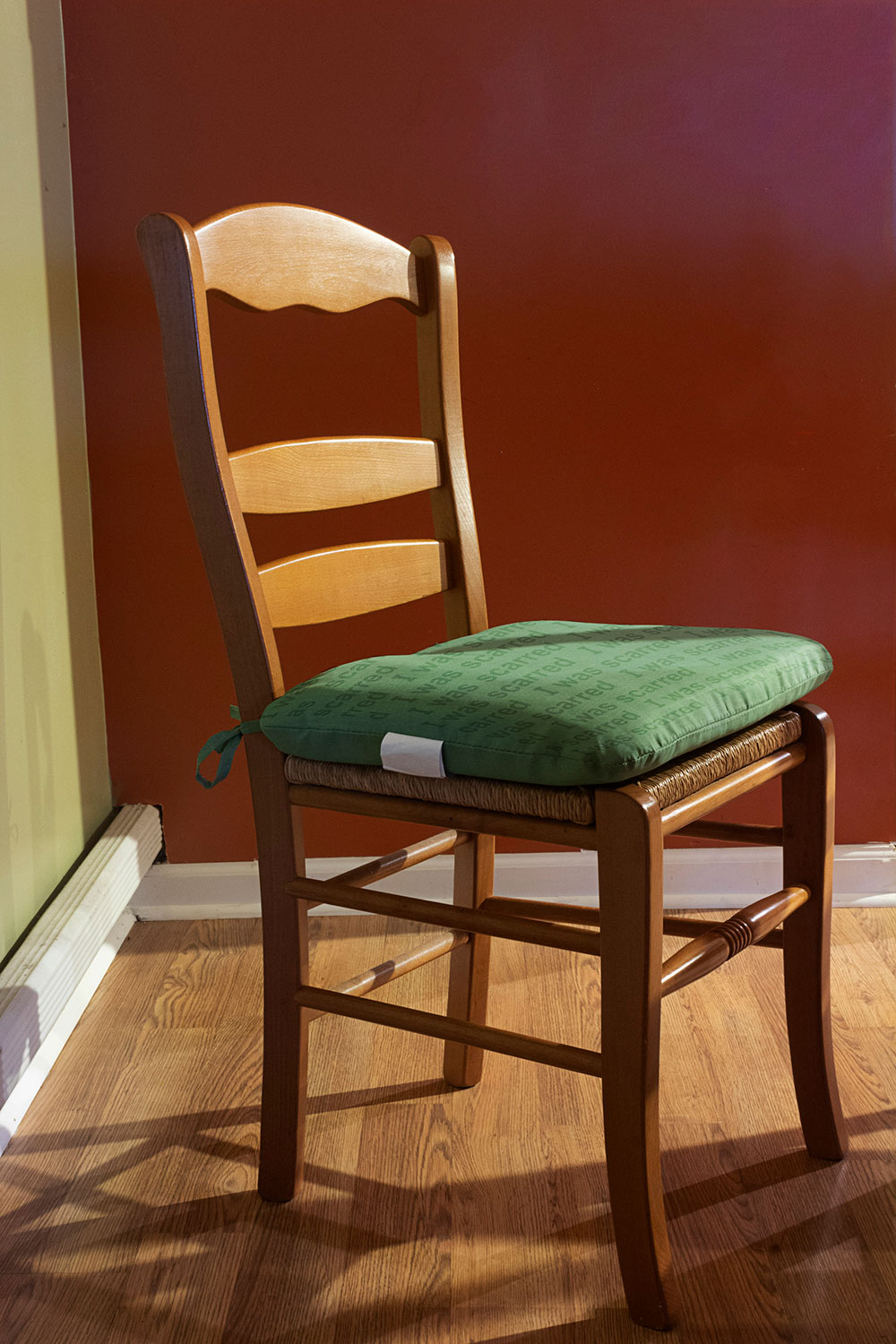wooden chair in corner with green pillow on it "I was scarred" written on pillow