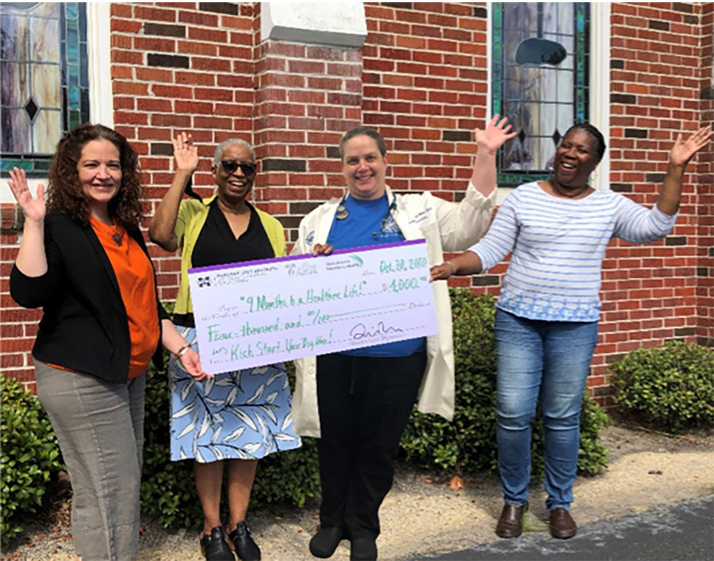 Pictured left to right, holding giant check and waving: Xenia Wickline (Program Believe), Alice Graham (Back Bay Mission), Wendy Williams (Coastal Family Health Center) and Kay Horne (Program Believe)