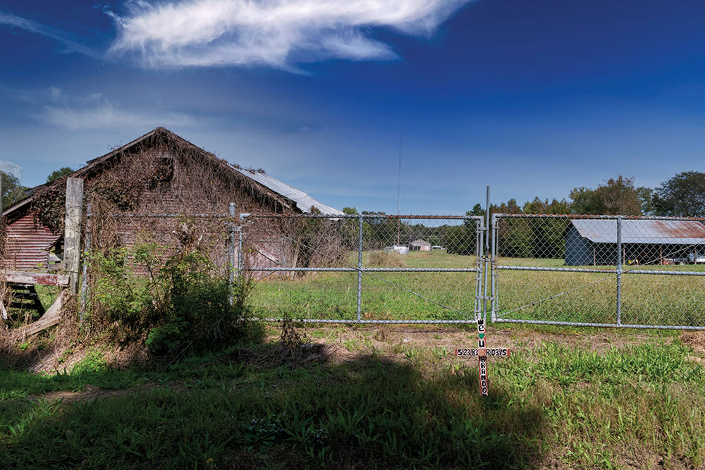 cross in front of fence that closes off old Barn/farm