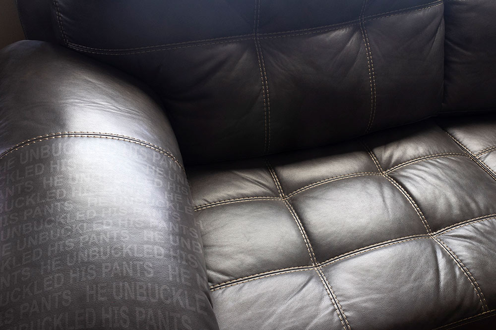 up close view of leather couch or chair "he unbuckled his pants" written on arm of chair on left
