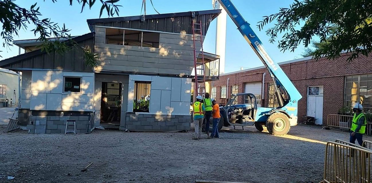 students wearing construction PPE and masks work on a modular building with blue crane 