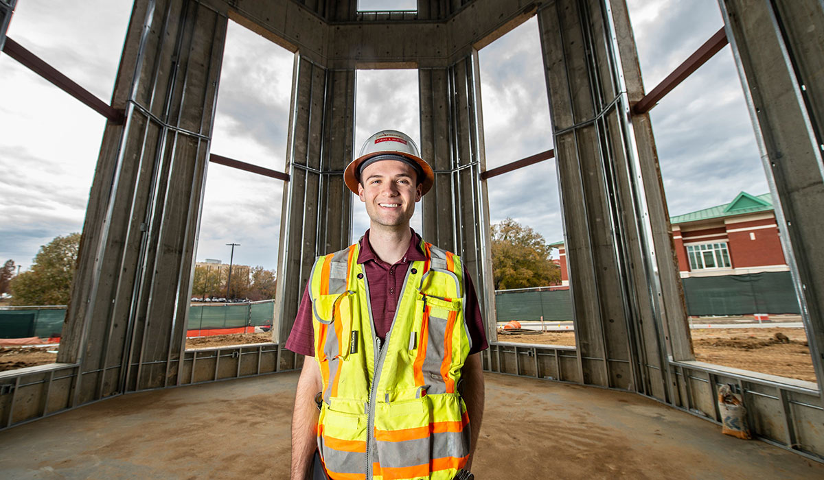 Hunter Bullock wearing hard hat and safety vest stands inside a building under construction on Mississippi State University's campus in Starkville