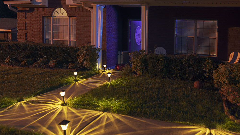 front of house at night with lights shining on sidewalk; purple light cast on partially open door of house