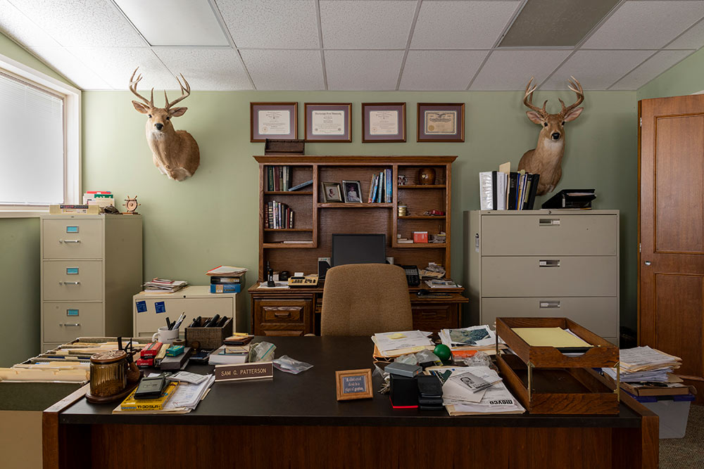 view of desk and back wall of an office, two deer heads frame top left and right of wall