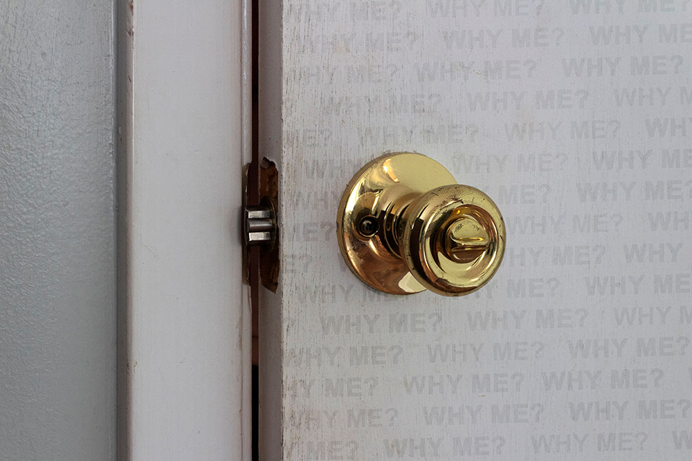 view of part of door with gold handle - door says "why me"
