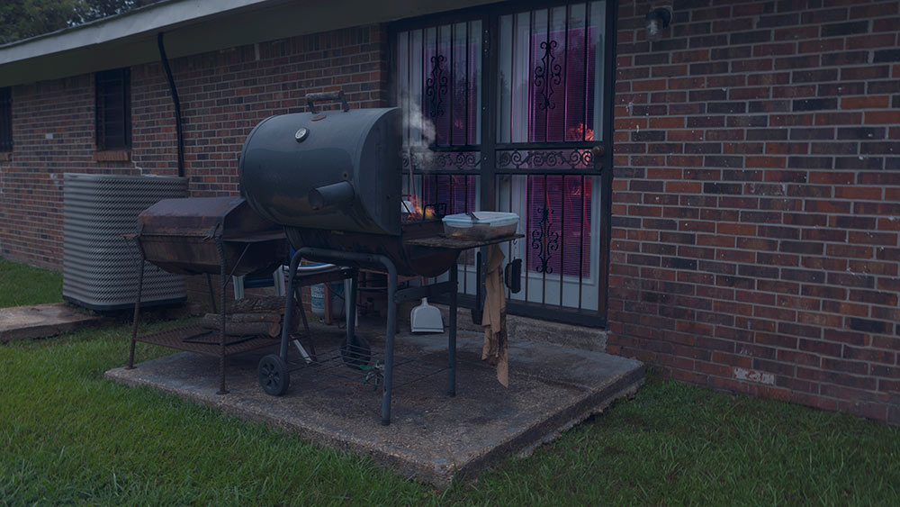 grll on patio outside of house; purple glow seen in glass door inside house