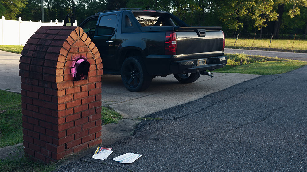 brick mailbox glowing pink at end of driveway; black truck sits in drive