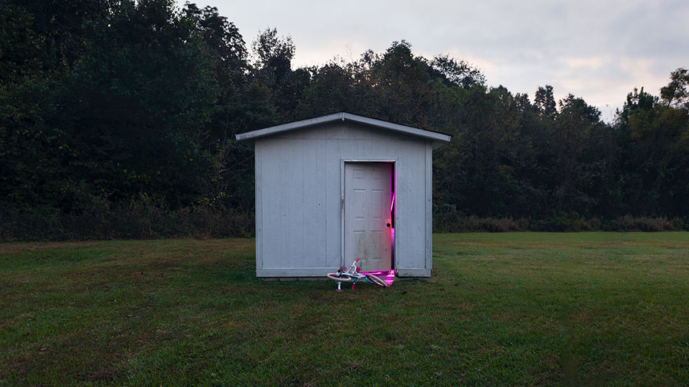 white shed in field with door slightly open and pink lights inside