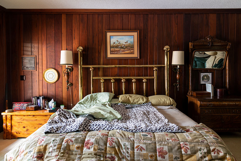 photograph of a bedroom with wood walls. view from foot of bed. gold headboard