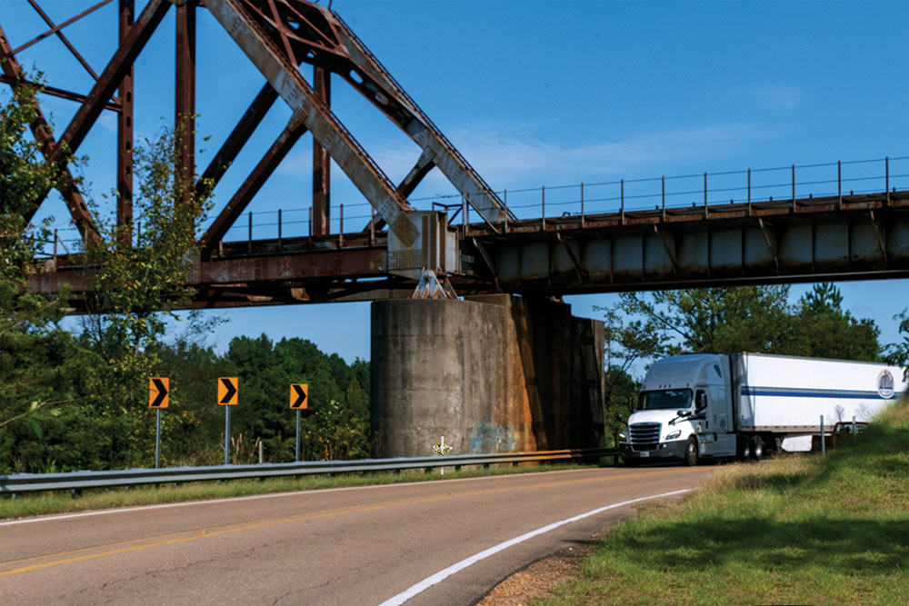 big truck is seen driving on a road under a metal bridge