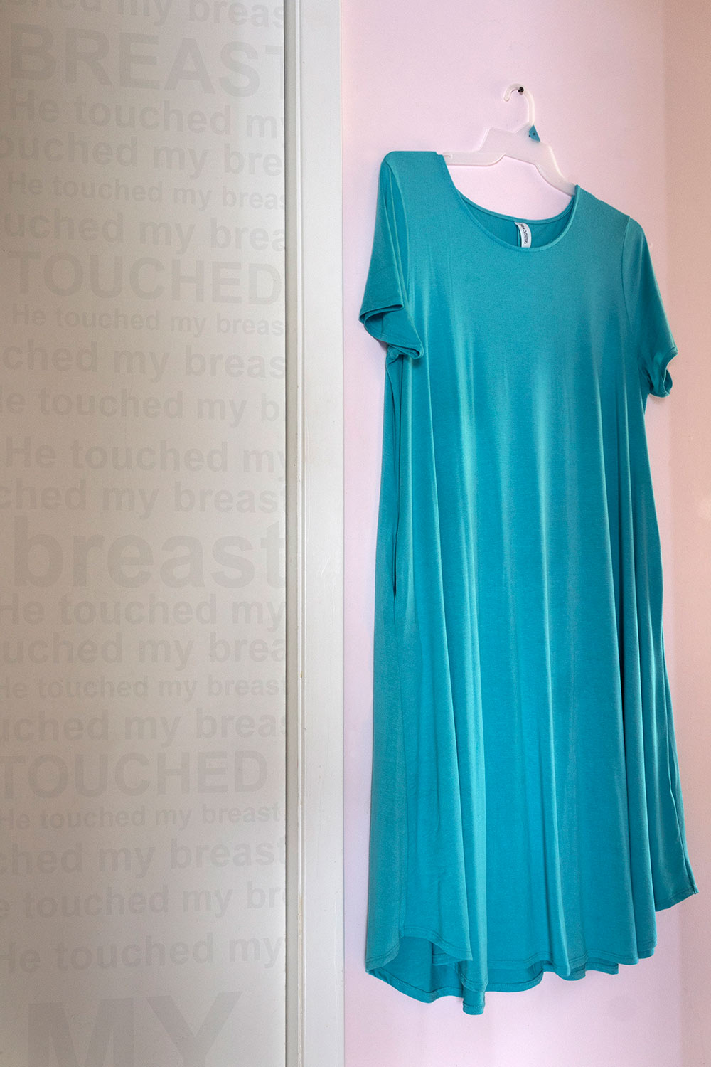 green dress on hanger - "He touched my breast" written on wall to left