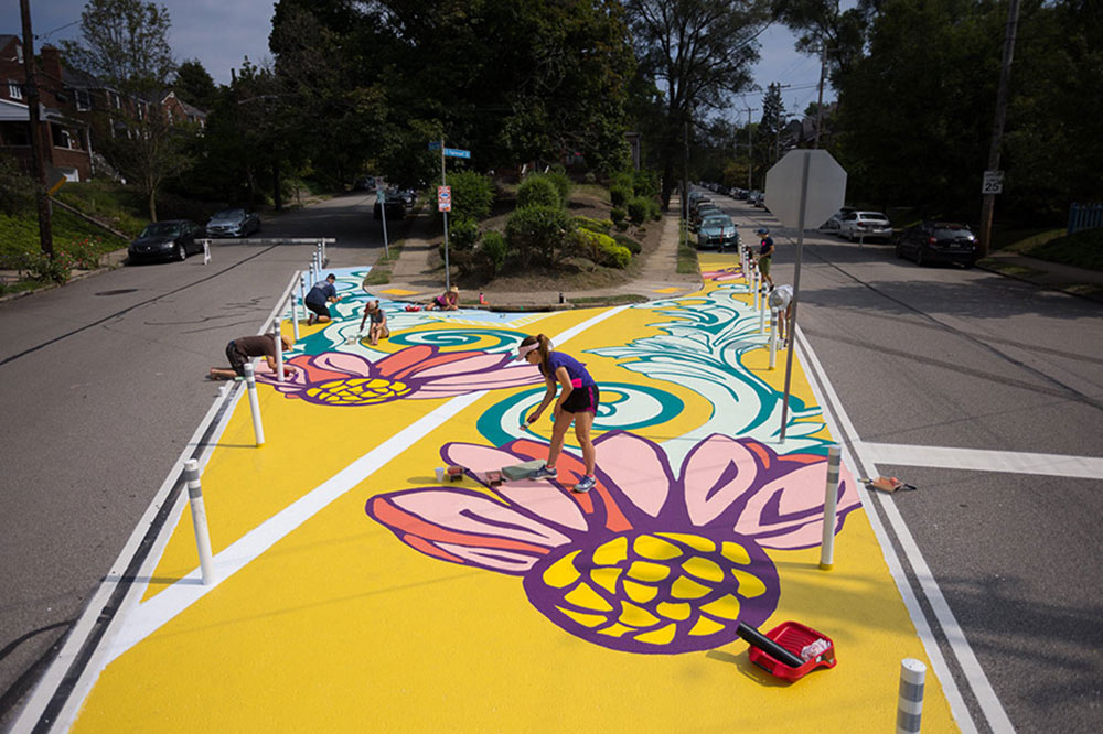 people paint yellow flower mural on street