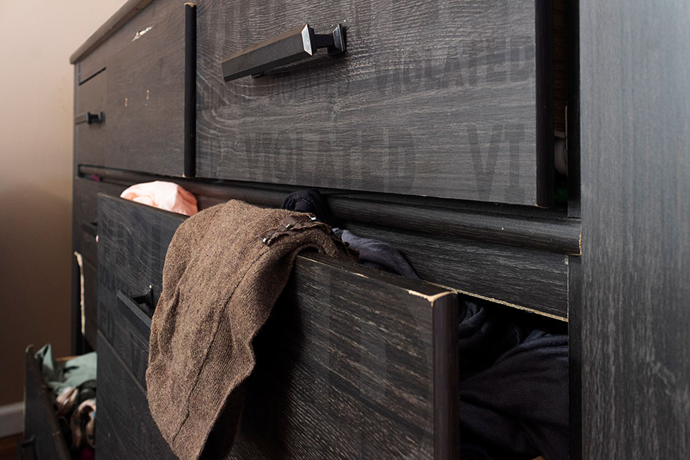 chest of drawers with brown sweater and other clothes hanging out; "violated" written on it