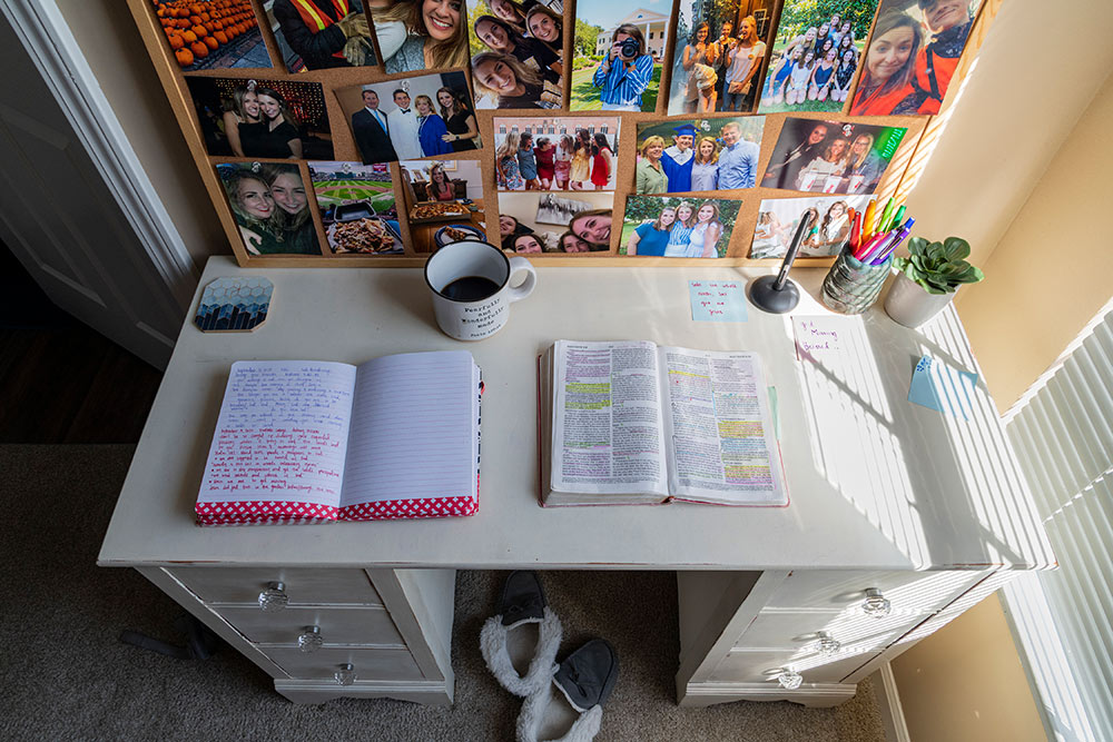 top view of desk with open journal and Bible and coffee on table, photos hang on wall behind