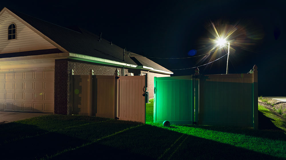 photo of house with right side fence opened to green glowing backyard