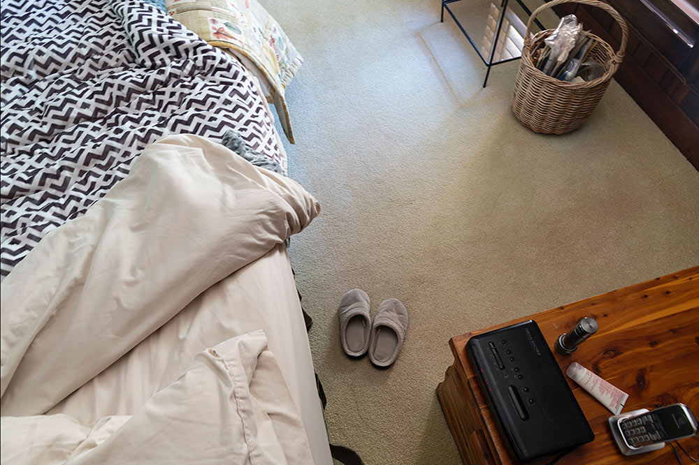 half view of bed from headboard above, slippers on floor and side table in view