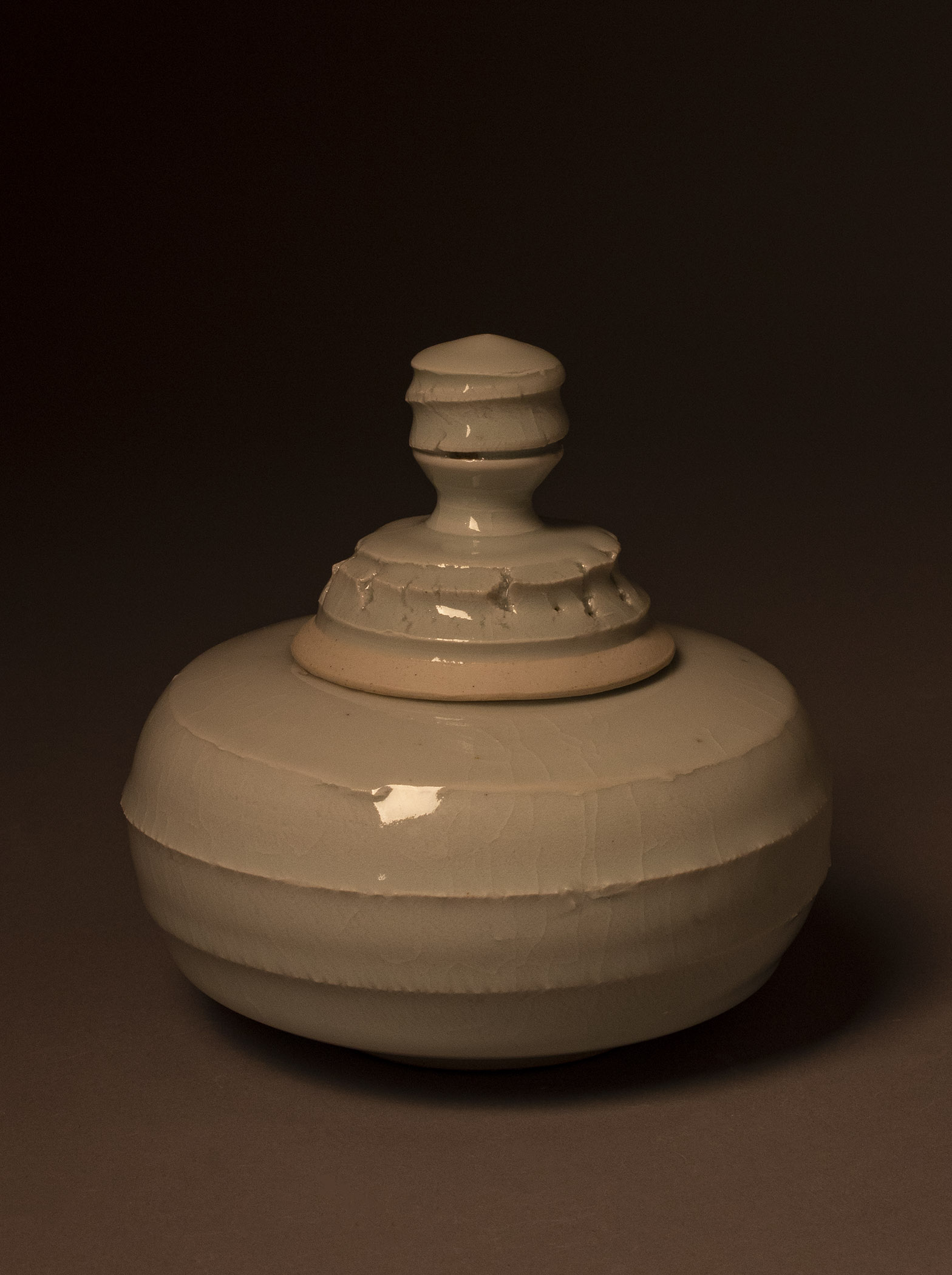 A similar shape to the one previously described, the textural element on the bottom of the jar is much more pronounced. While the shoulder of the piece is smooth and nearly flat, the body of the jar has a texture that might resemble a craggy rockface or even something akin to the tread on a dry-rotting tire. Like the other porcelain pieces, the glaze is glassy and relatively smooth.