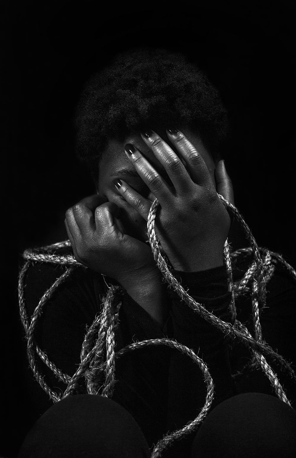 black and white shot of female with hands holding ropes and covering face