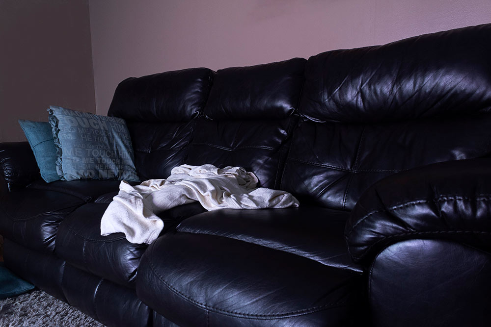 black leather couch with white blanket and teal pillows at left side "he had me touch him" written on pillow