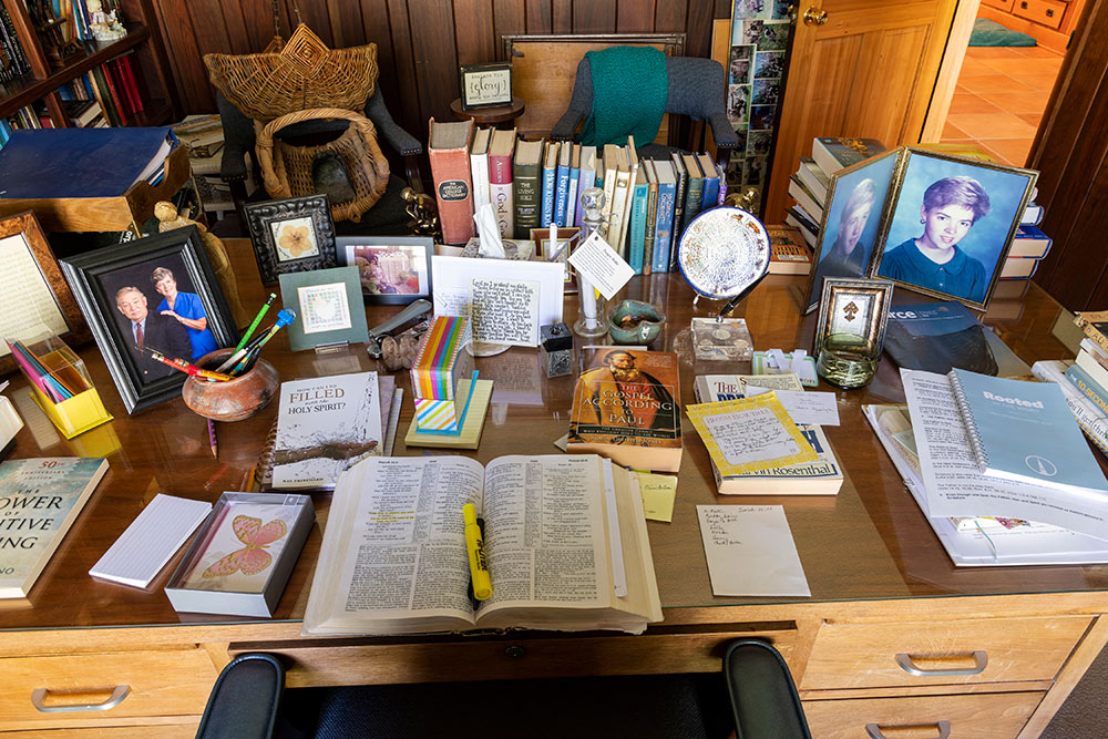 cluttered desk with books and photos and open Bible with highlighter