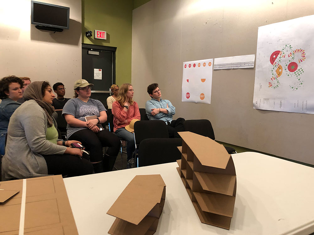 architecture students look at a wall with a design taped on it