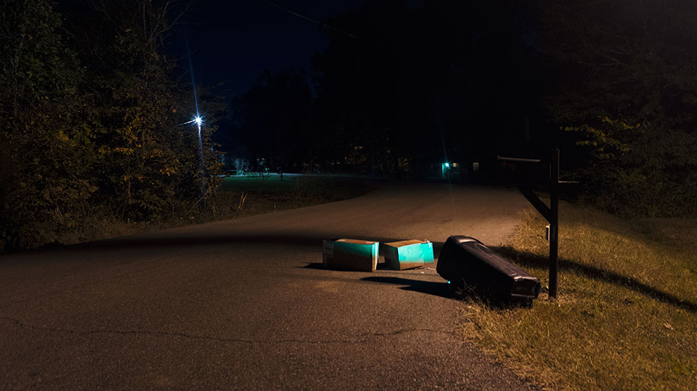 trash can turned over in road, 2 boxes with green lights on them lay in front