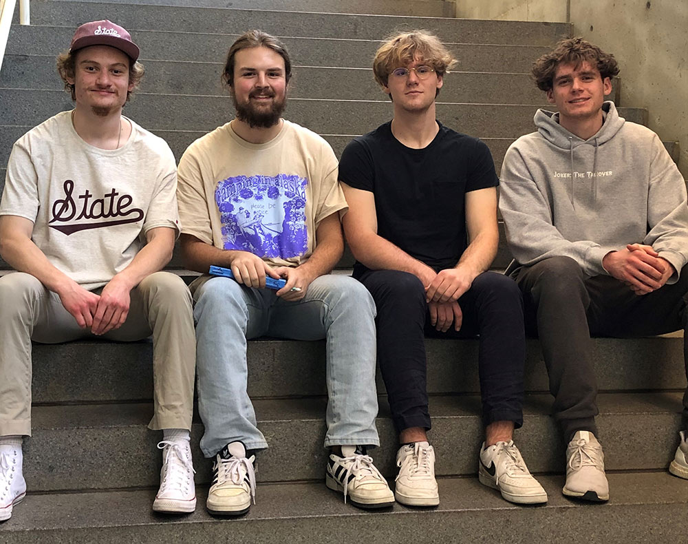 students sit on steps: left to right: Alaster Redmond, John Michael Gray, Peter Fox and Ryan Kubinski 