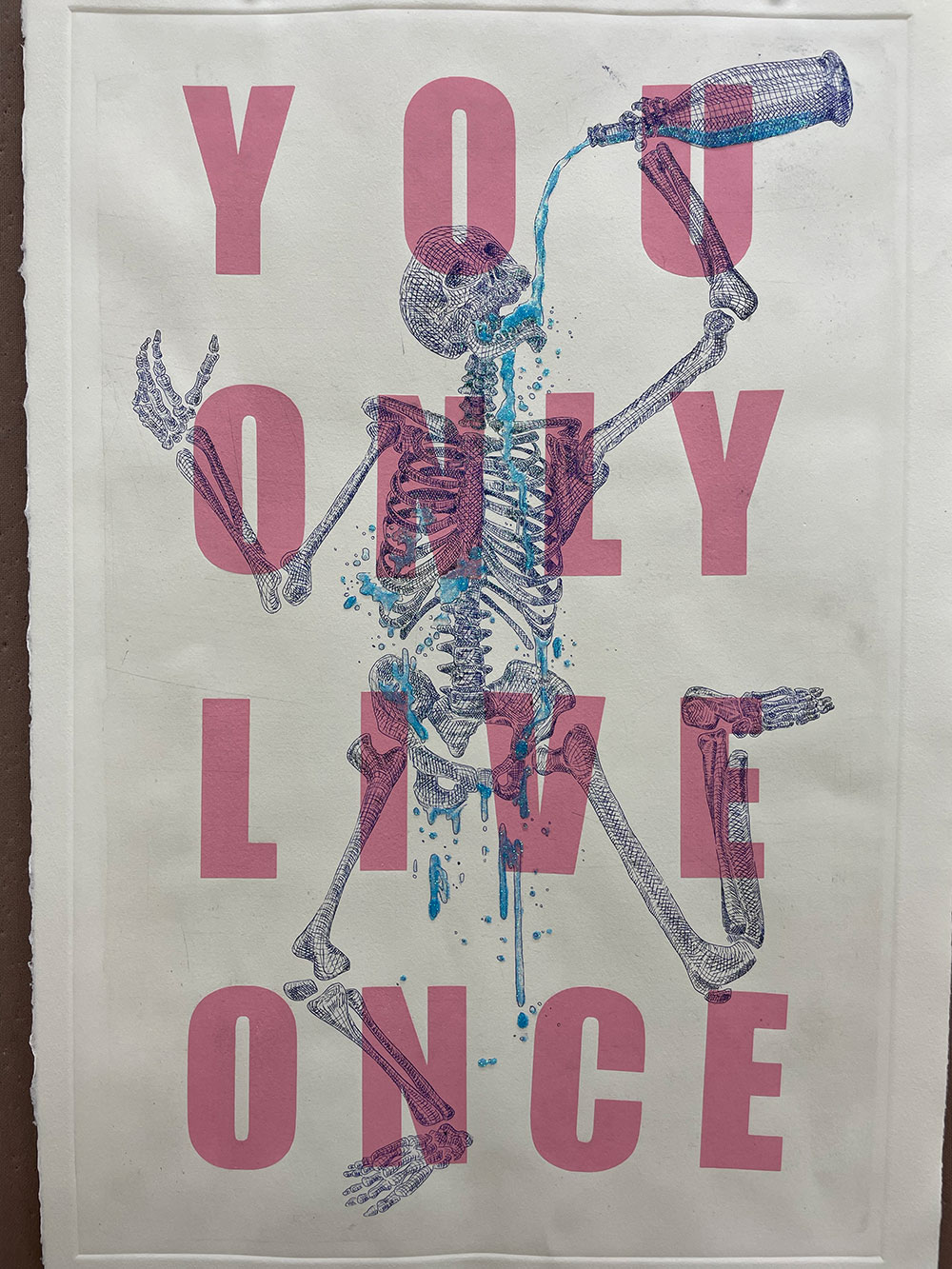 A colored printed image of a dancing skeleton pouring a drink down his throat with the words written across "You only live once"