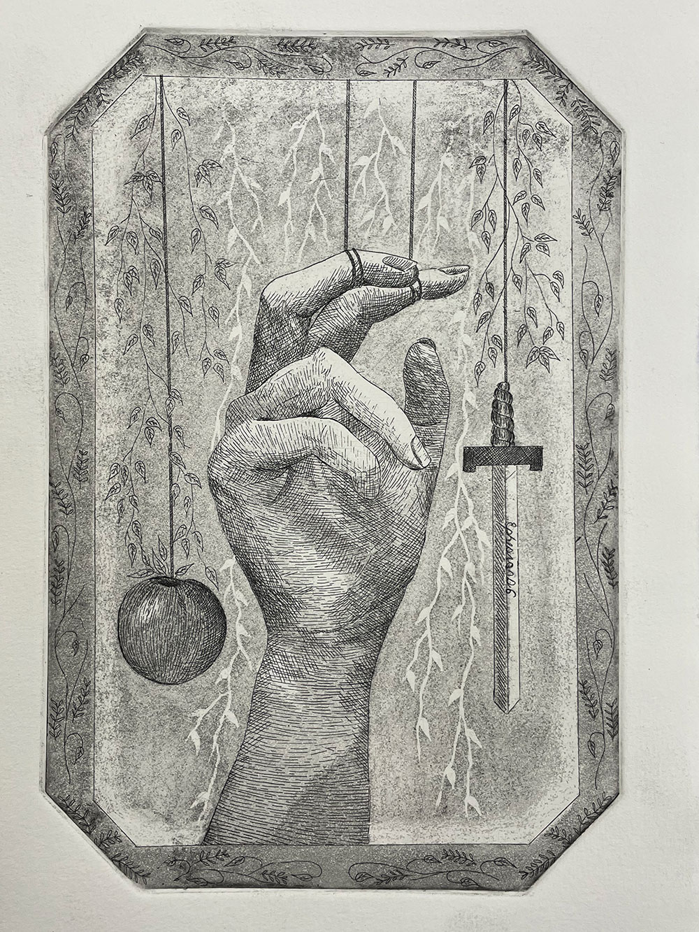 A printed image of a hand wit two fingers attached to string holding a sword and an apple