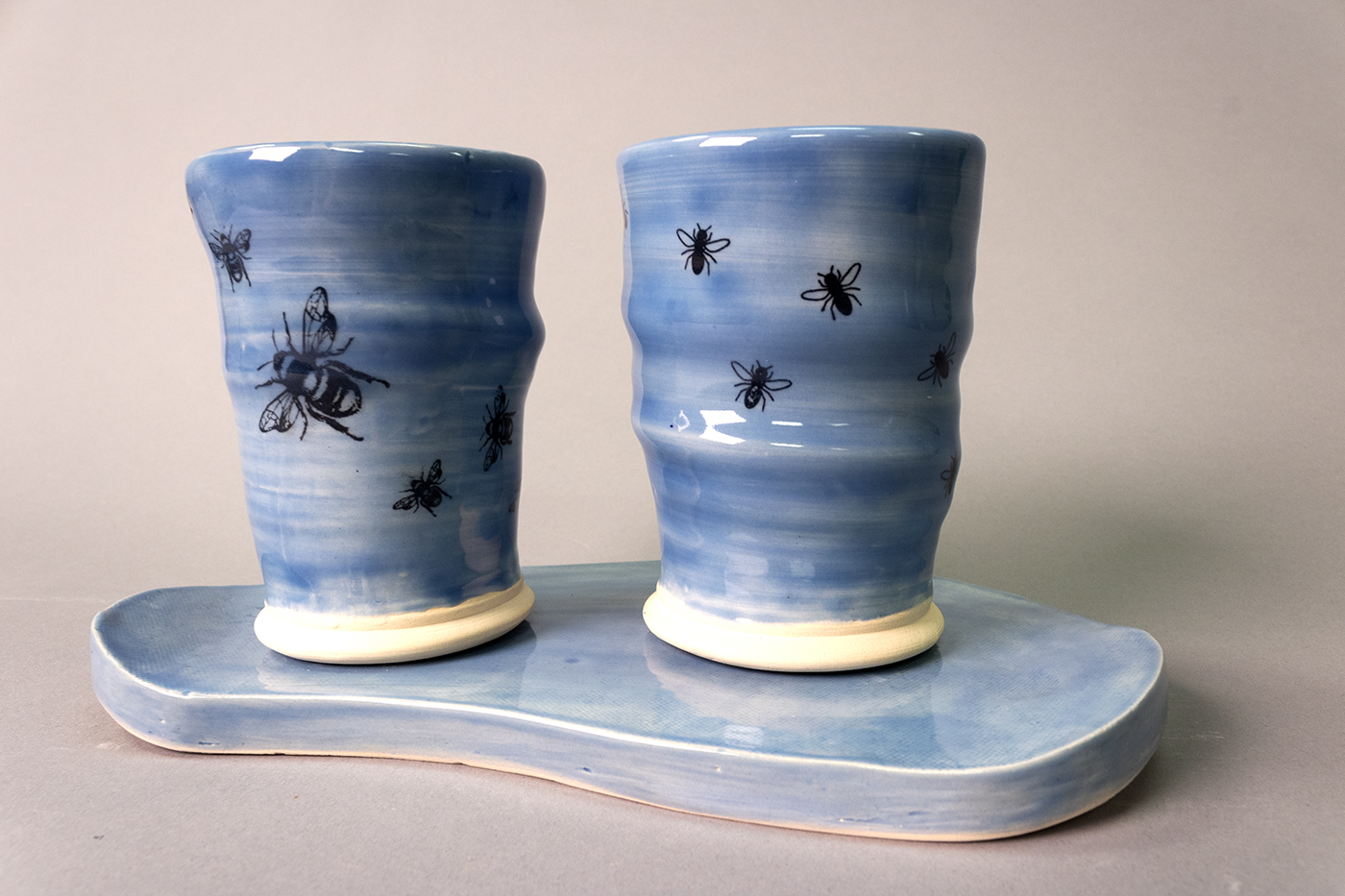 Two blue cups with images of flies and bees sitting a coordinating tray.