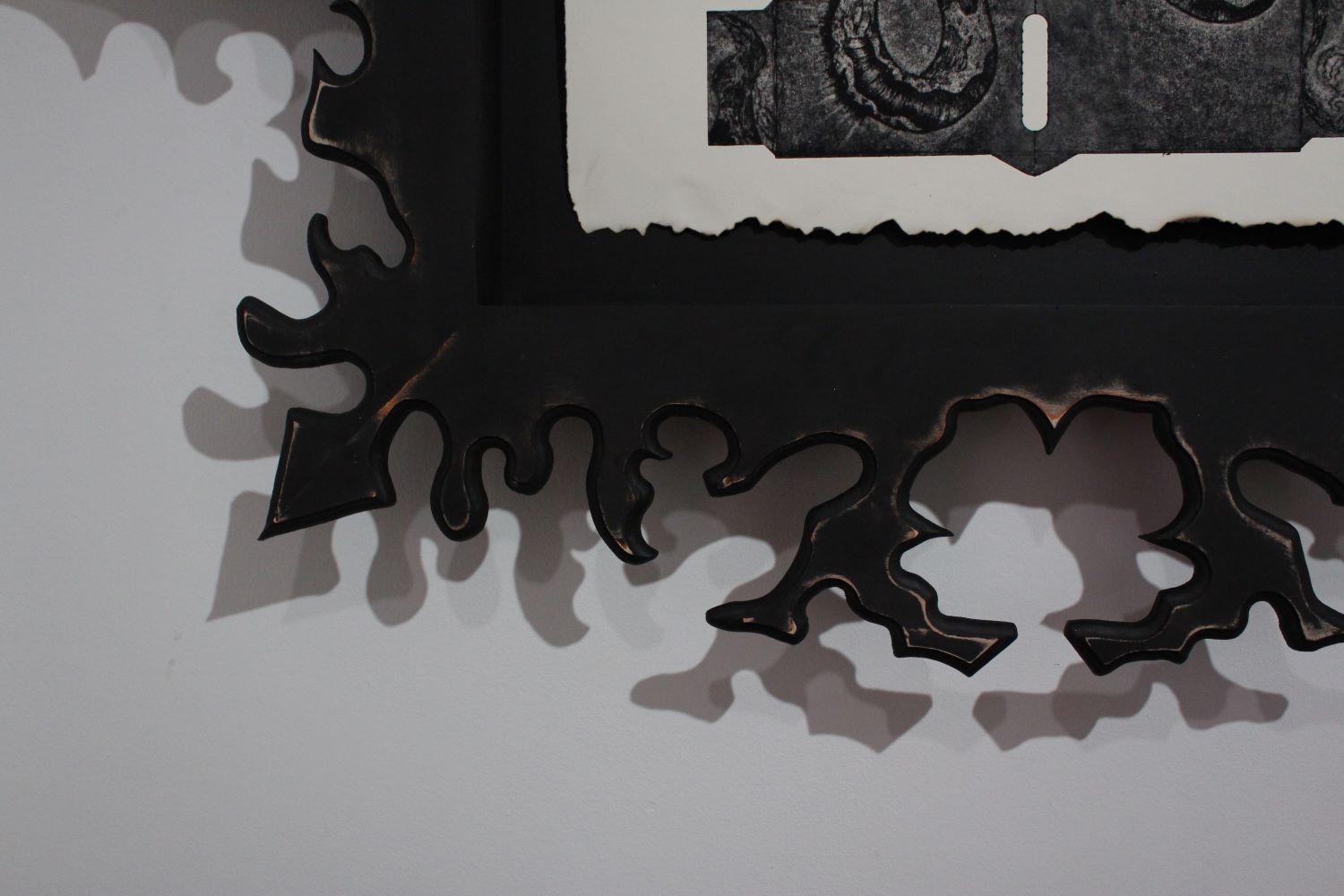 Close up shot of  Come, My Sister. Bottom left corner of frame and print with organic points, drips, and branches cut and routed out of the face fram. Painted black, then sanded to appear distressed. Inset into the frame/shadowbox, the bottom edge of the dark greyscale print, have burned paper edges.  