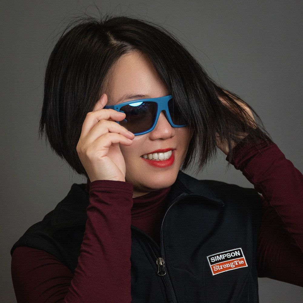 Bonnie Yang poses holding on to blue sunglasses