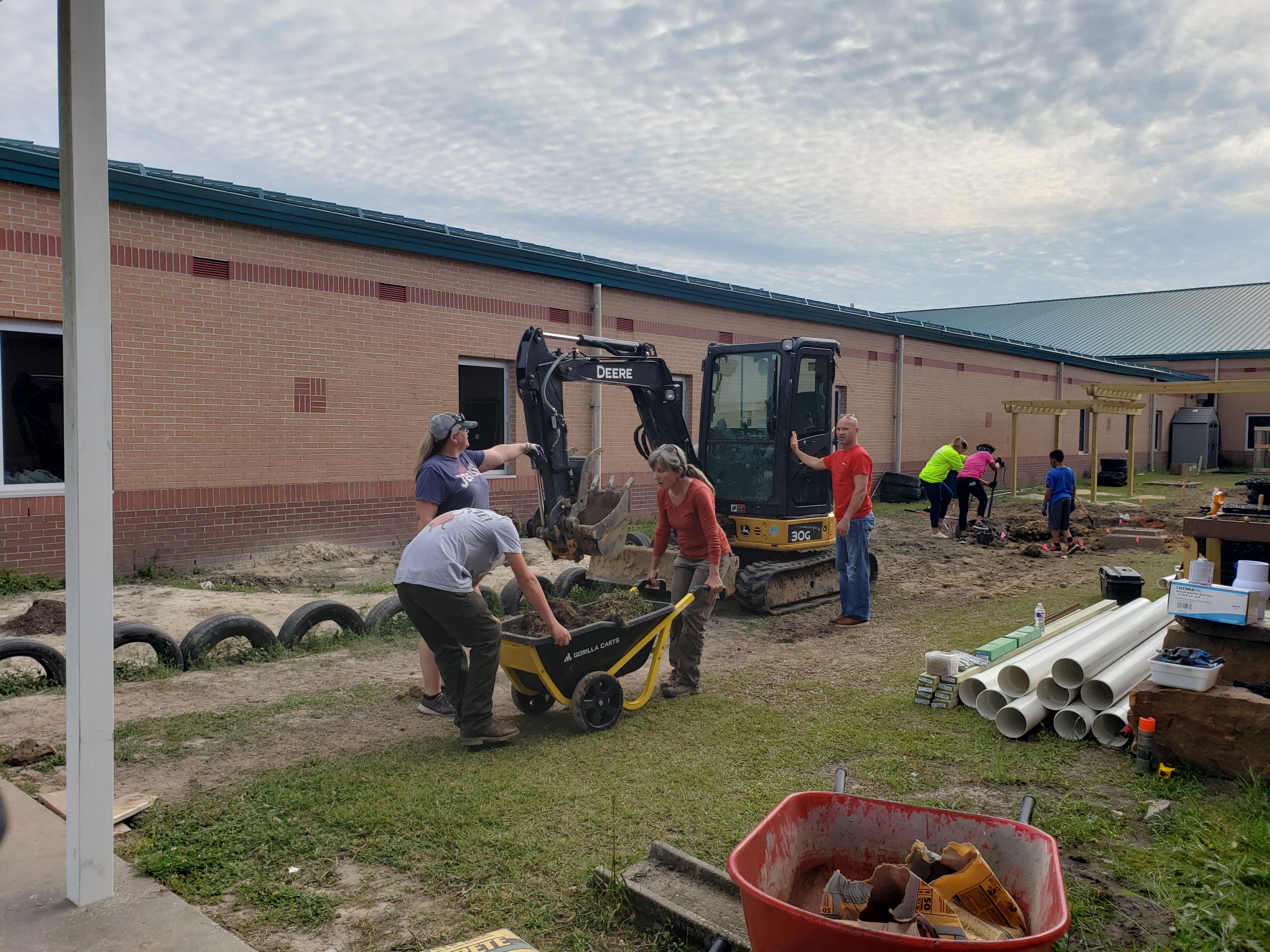 people work on project. 2 people with wheel barrel, a tractor in back