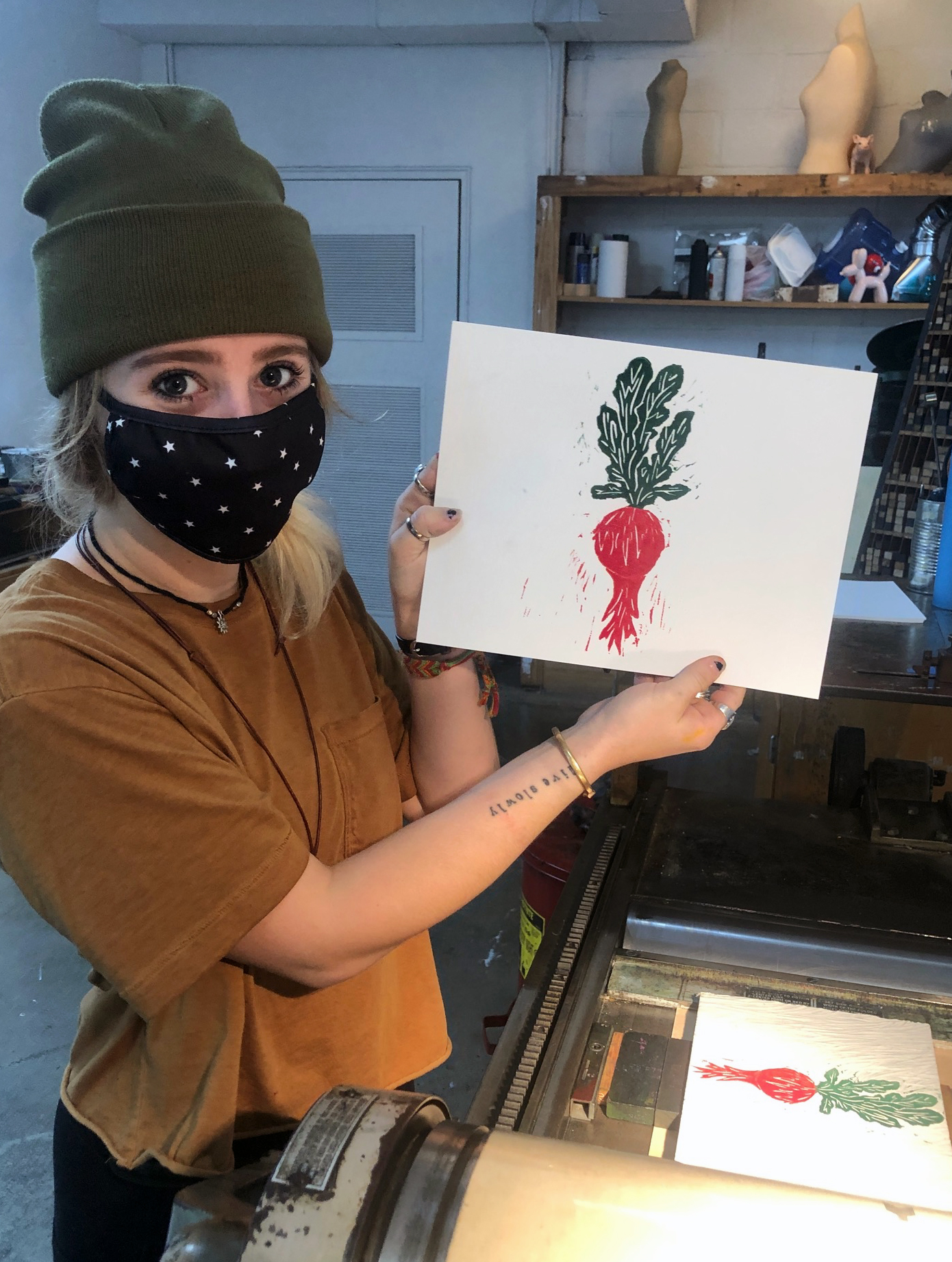 Photograph of a student holding up a print image of a red beet with green leaves.